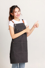 Smiling young Asian woman entrepreneur wearing cooking apron show trump up working part-time on isolated background. Small business and startup concept.