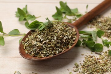 Dried oregano in spoon and green leaves on wooden table, closeup