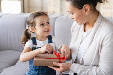 Wall Mural - Caucasian young mother unwrapping opening unpacking birthday Christmas New Year Mother`s day present with her small daughter child girl. Family celebration holiday