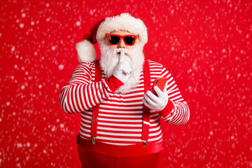 Wall Mural - Portrait of his he nice handsome mysterious bearded fat Santa using device app 5g shopping secret sale discount showing shh sign silence mute isolated bright vivid shine vibrant red color background