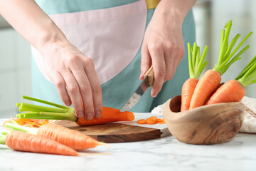 Poster - Woman cutting fresh carrot at white marble table, closeup