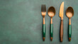 © Nano Photos - A stylish set of gold cutlery with green handles, featuring a fork, two spoons, and a knife, neatly arranged on a textured green surface.