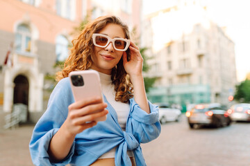 Young woman walking around old street and using smartphone. Online Communication with friends. Technology, connection, blogging, modern lifestyle concept.