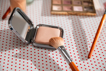 Makeup essentials: compact powder and brush on a stylish polka dot surface, capturing the essence of beauty accessories and cosmetics for a perfect makeup routine.