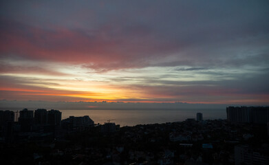 City skyline with buildings silhouetted against vibrant sunrise over the sea. Aerial view at dusk