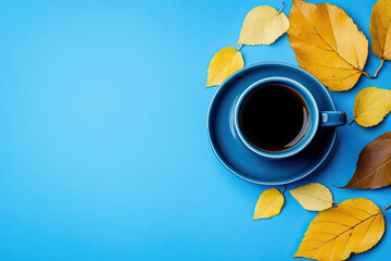 Blue saucer and cup of black coffee with yellow leaves next to it on a blue background with copy space