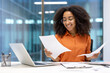 © Liubomir - Smiling woman reviewing documents at office desk with laptop and glasses