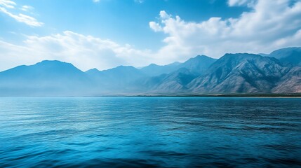  A breathtaking view of a mountain range across a calm blue ocean with a bright blue sky above.