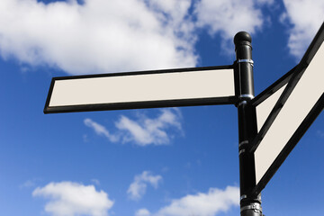 Black pole with blank street signs. Directional markers against a backdrop of blue sky and clouds. White copy space metal frames. Crossroad background. Choosing direction guidance.