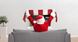 © Ljupco Smokovski - Santa Claus cheering with a scarf and sitting on a sofa in front of tv