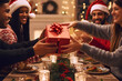 © Neitiry - Happy, smiling diverse group of friends exchanging christmas gifts, presents, cheerful young people celebrating christmas, new year eve, having fun on a festive home party at the dinner table.