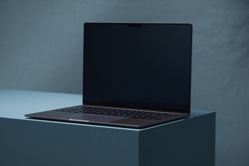 sleek laptop on a blue platform: a modern laptop with a black screen rests on a minimalist blue plat