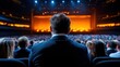 © Anna - A lone figure in formal attire sits in a theater, gazing towards the illuminated stage, surrounded by an audience eagerly anticipating a live performance on a lively night