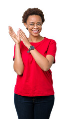 Wall Mural - Beautiful young african american woman wearing glasses over isolated background Clapping and applauding happy and joyful, smiling proud hands together