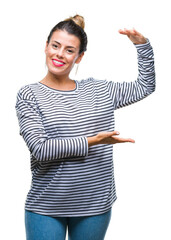 Wall Mural - Young beautiful woman casual stripes sweater over isolated background gesturing with hands showing big and large size sign, measure symbol. Smiling looking at the camera. Measuring concept.