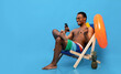 © Prostock-studio - Online summer sale. Carefree black man holding credit card and smartphone, shopping on web in lounge chair, blue background, panorama with empty space. Handsome young guy purchasing goods on internet