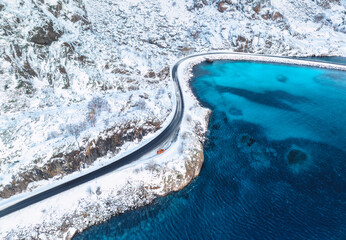 Wall Mural - aerial view of curved snowy road to the island and blue sea at sunset. highway in snow and azure tra