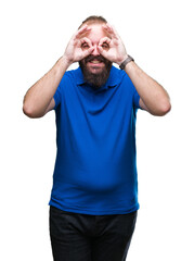 Wall Mural - Young caucasian hipster man wearing blue shirt over isolated background doing ok gesture like binoculars sticking tongue out, eyes looking through fingers. Crazy expression.