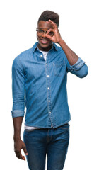 Wall Mural - Young african american man over isolated background doing ok gesture with hand smiling, eye looking through fingers with happy face.