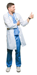 Wall Mural - Handsome doctor man wearing medical uniform over isolated background Looking proud, smiling doing thumbs up gesture to the side