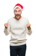 © Krakenimages.com - Young handsome man wearing santa claus hat over isolated background celebrating surprised and amazed for success with arms raised and open eyes. Winner concept.