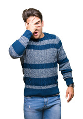 Wall Mural - Young handsome man over isolated background peeking in shock covering face and eyes with hand, looking through fingers with embarrassed expression.