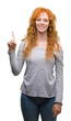 © Krakenimages.com - Young redhead woman showing and pointing up with finger number one while smiling confident and happy.