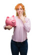 © Krakenimages.com - Young redhead woman holding piggy bank cover mouth with hand shocked with shame for mistake, expression of fear, scared in silence, secret concept