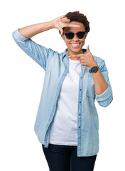 Wall Mural - Beautiful young african american woman wearing sunglasses over isolated background smiling making frame with hands and fingers with happy face. Creativity and photography concept.