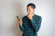 © Tito Rollis - Young men wearing green flannel covering his mouth while looking smartphone on isolated white background