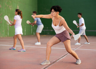 Wall Mural - Portrait of sporty young girl playing paleta fronton on outdoor court, ready to hit ball. Healthy and active lifestyle concept