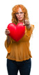 © Krakenimages.com - Young redhead woman in love holding red heart pointing with finger to the camera and to you, hand sign, positive and confident gesture from the front