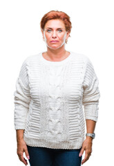 Wall Mural - Atrractive senior caucasian redhead woman wearing winter sweater over isolated background with serious expression on face. Simple and natural looking at the camera.