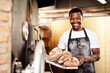 © HockleyM4/peopleimages.com - Happy, portrait and black man with bread at bakery for pastry, production or handmade cuisine at shop. Young African, male person or baker with smile, loafs or rolls for food, delicacy or produce