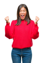 Wall Mural - Young asian woman wearing winter sweater over isolated background celebrating surprised and amazed for success with arms raised and open eyes. Winner concept.