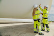 © ultramansk - Two engineers in high-visibility gear inspect a large wind turbine blade at a construction or installation site. renewable energy, wind power, and the detailed work involved in energy projects.