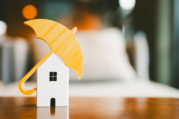 Wall Mural - Model of umbrella with house on wooden table concept of the system of insurance savings and Housing insurance against impending loss and fire, building fire insurance concepts.