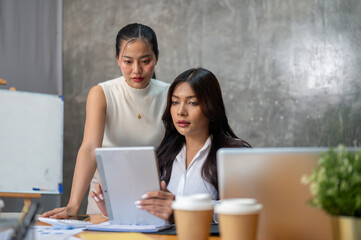 Two gorgeous Asian businesswomen are focused on working on a business project together in the office