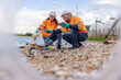 © kamonrat - Two environmental management experts wearing protective gear such as hard hats, gloves and reflective vests analyze coastal waste and industrial wastewater.