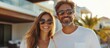 © MBRAMO - Happy couple wearing sunglasses standing in front of a modern home.
