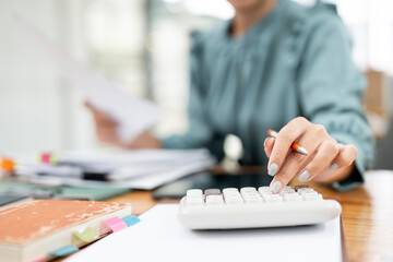 Close-up of businesswoman hands using a calculator to check company finances. Business woman calculating monthly expenses, managing budget, papers, loan documents, invoices.