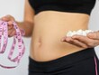 © Nadzeya - A woman holding a measuring tape in one hand and weight loss supplements in the other, highlighting body fitness