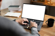 © NAMPIX - Close-up image of a man working on laptop computer at a table, typing on the laptop keyboard. the laptop with a white screen mockup