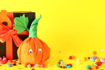 Sticker - Paper pumpkin for Halloween, gift box and tasty candies on yellow background, closeup