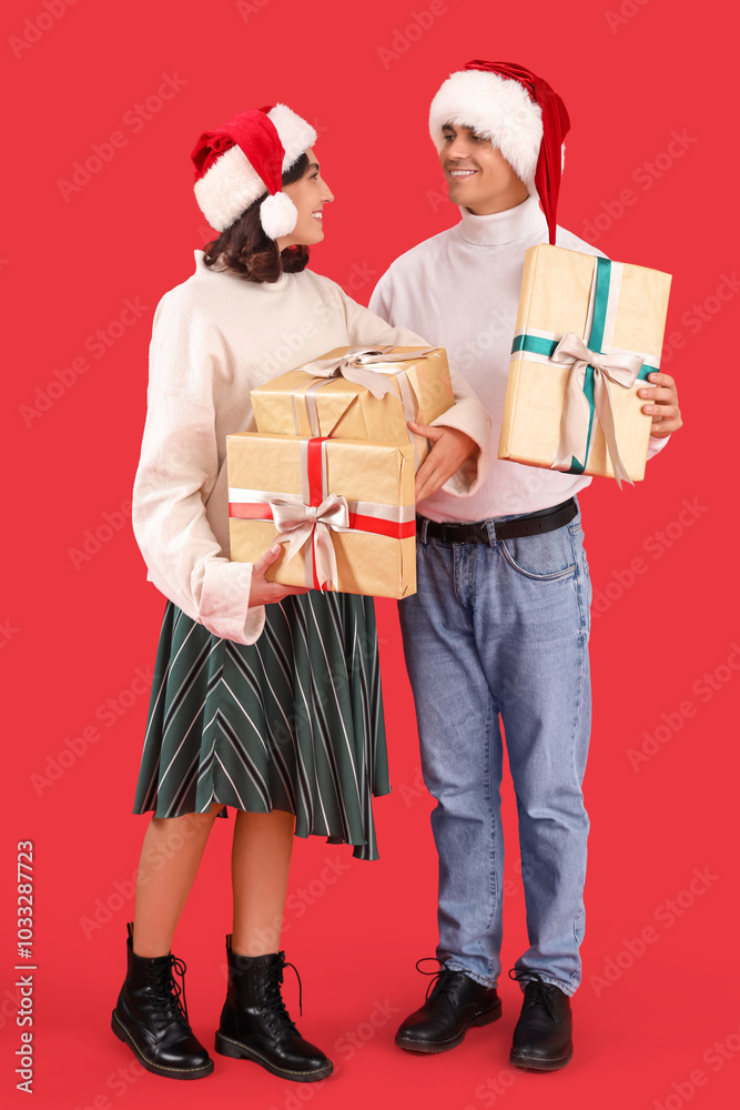 Happy young couple in Santa hats with gift boxes on red background