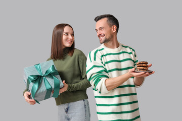 Young couple with gift box and plate of tasty cookies on grey background