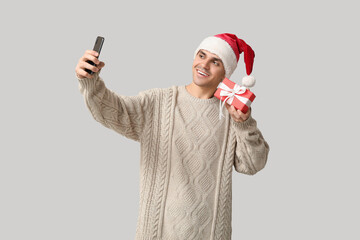 Sticker - Handsome young man in Santa hat with Christmas gift taking selfie on white background