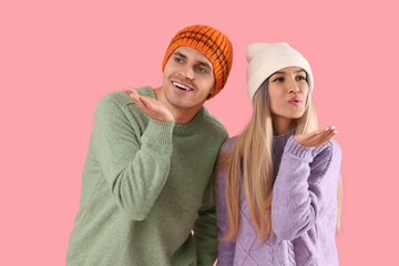 Poster - Happy young couple in winter clothes blowing kisses on pink background