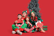 © Pixel-Shot - Happy family in elf's costumes with gift boxes, cards to Santa and Christmas tree on red background