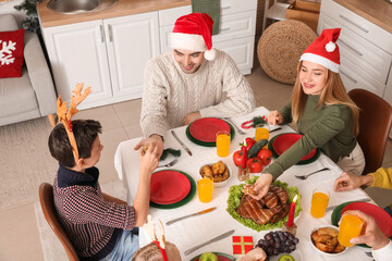 Canvas Print - Happy family in Santa hats having dinner at home on Christmas eve